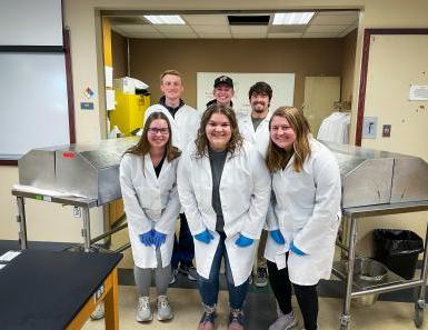 Biology students wearing white coats pose for a picture in the lab